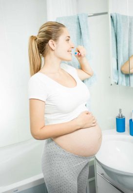 Pregnant woman brushes her teeth in front of mirror