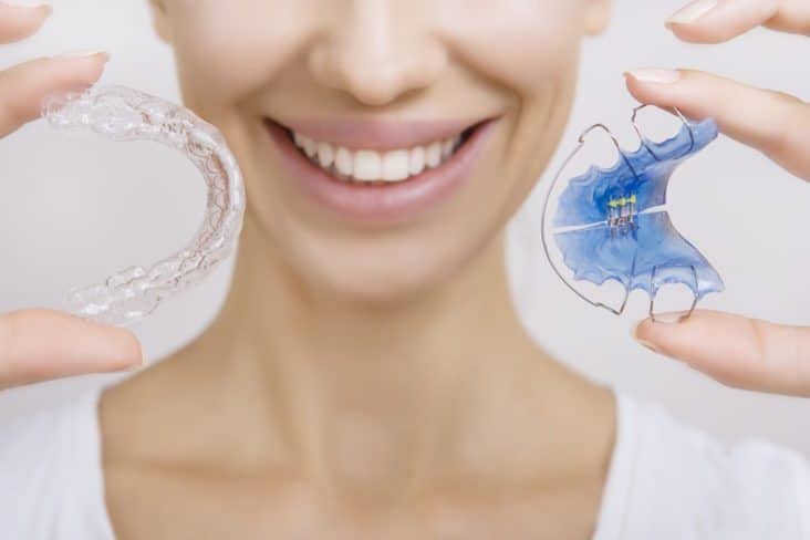 A smiling girl holding a retainer and an aligner